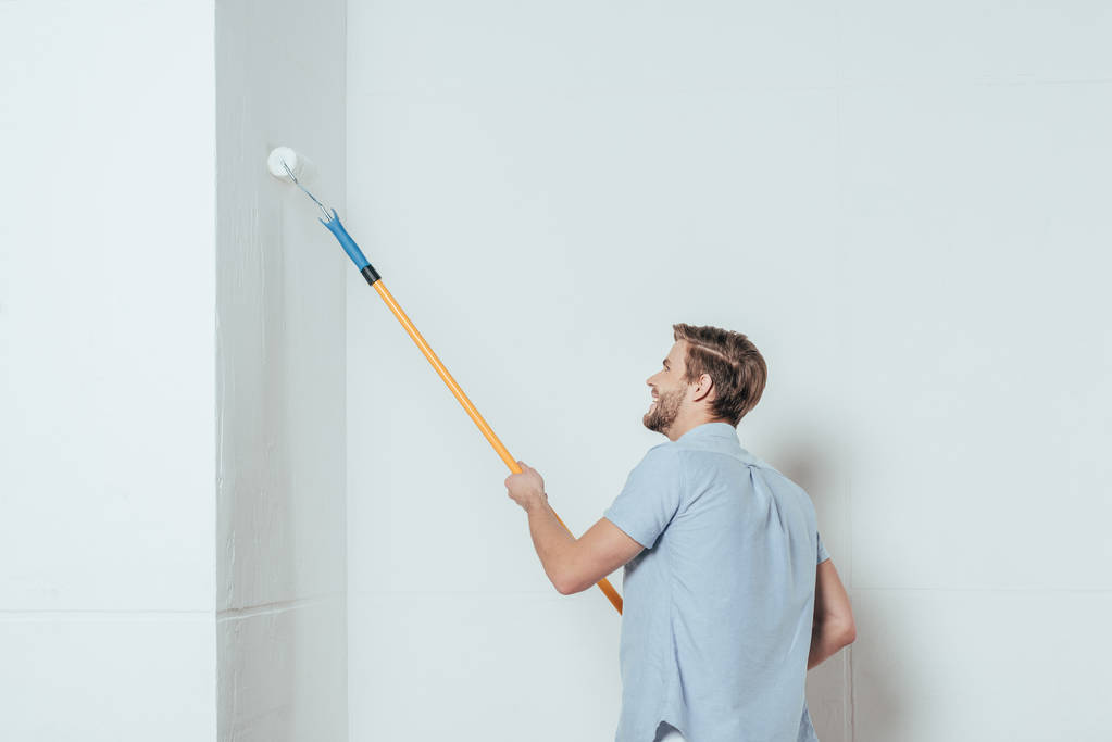 vista laterale del giovane sorridente che utilizza rullo di vernice mentre dipinge la parete a casa
 - Foto, immagini