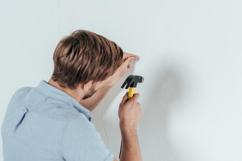 Rückansicht eines jungen Mannes, der zu Hause Nagel in Wand hämmert - Foto, Bild