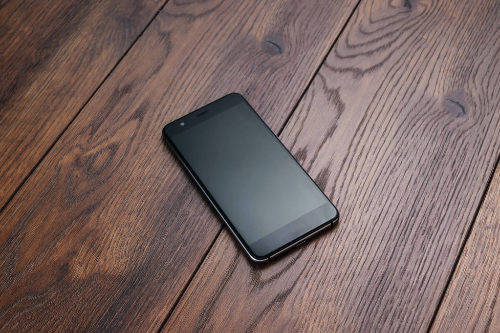 Современный смартфон лежит на коричневом деревянном столе. Копирование пространства
. - Фото, изображение