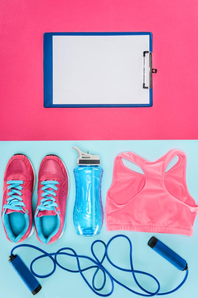Sportapparatuur met schoenen, touw, sports shirt en Klembord geïsoleerd op roze en blauw overslaan - Foto, afbeelding