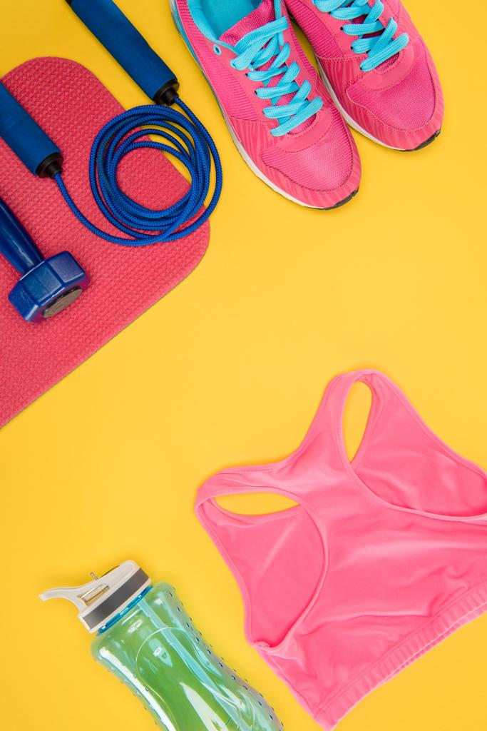 Sports equipment with shoes, dumbbell, sports top and skipping rope isolated on yellow - Photo, Image