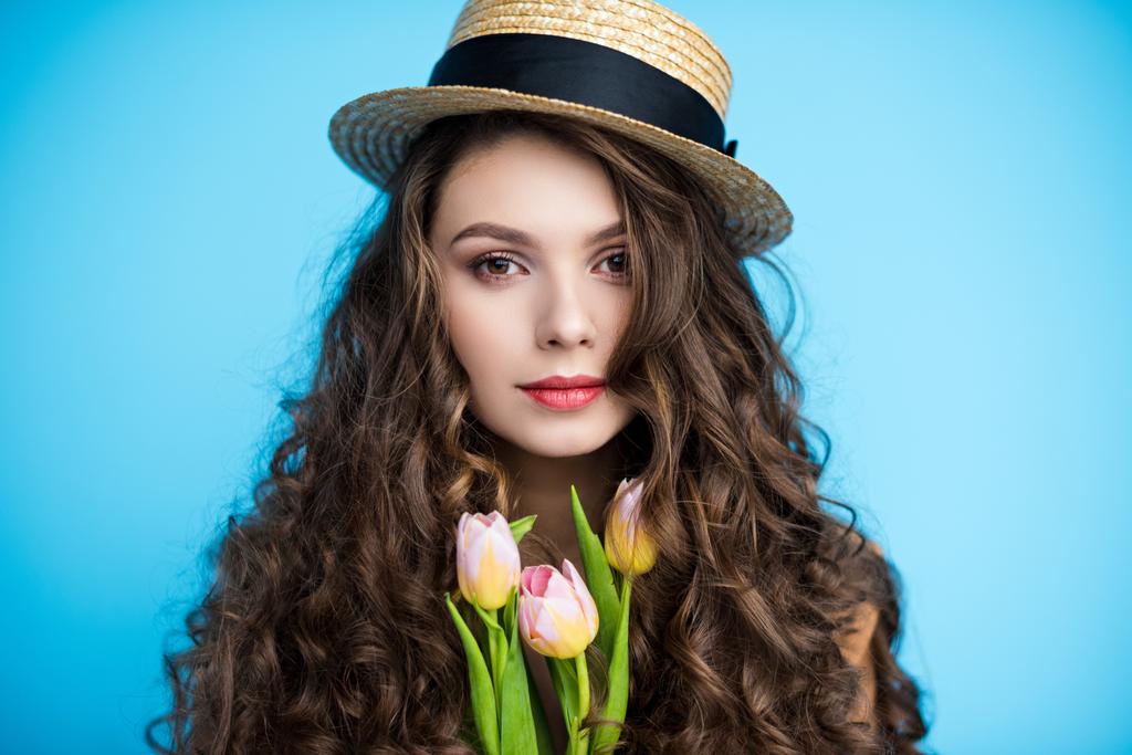 aantrekkelijke jonge vrouw met lang krullend haar in canotier hoed houden van mooie tulpen - Foto, afbeelding