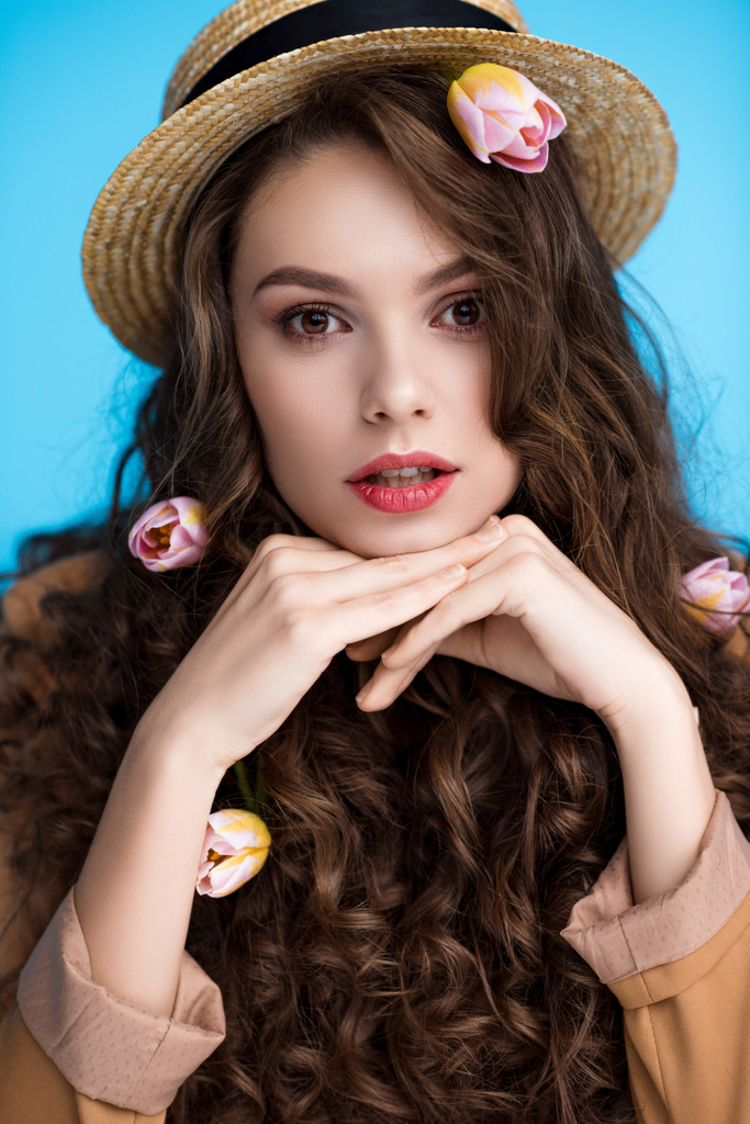 schöne junge Frau mit Kanuhut und Blumen im langen lockigen Haar, die in die Kamera schaut - Foto, Bild