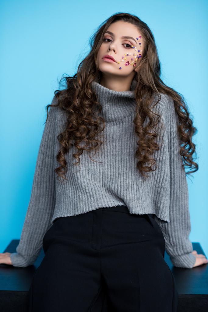 молода жінка з квітами на обличчі в стильному светрі, сидить на столі
 - Фото, зображення