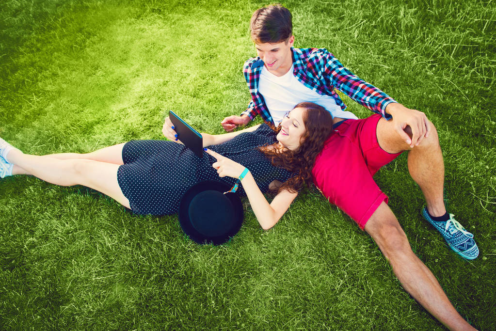 Двоє молодих людей розслабляються на траві з планшетом
 - Фото, зображення
