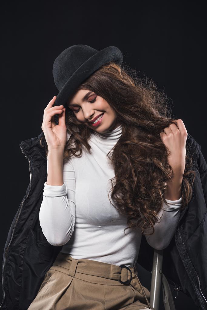 mosolygó fiatal nő, elegáns kalapját, és ül a létra elszigetelt fekete téli kabát - Fotó, kép