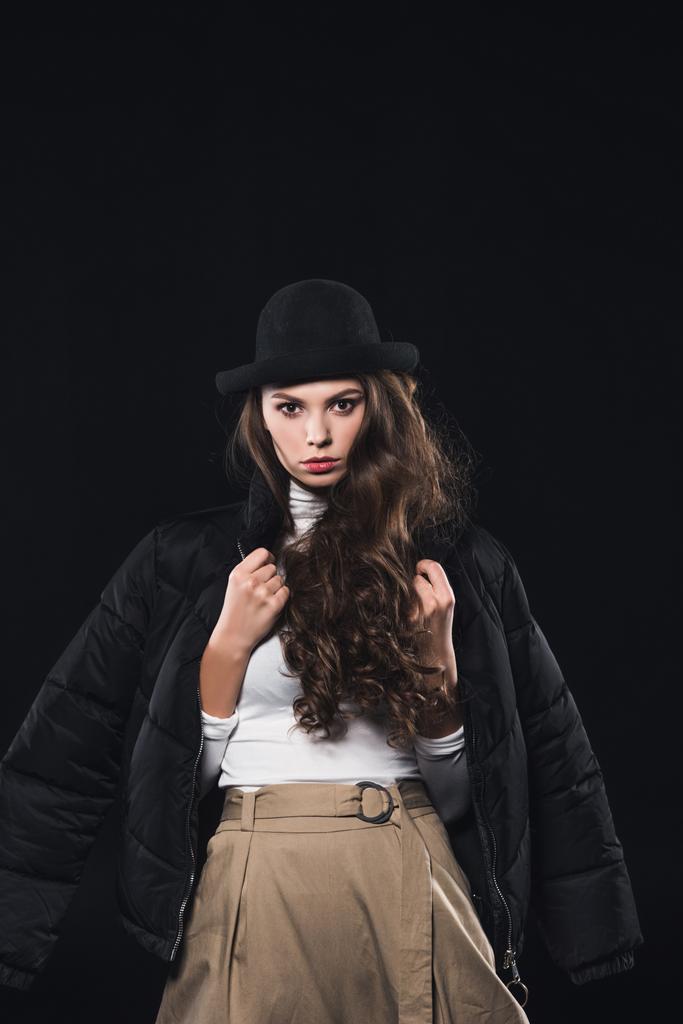 Porträt einer schönen Frau mit Hut und Winterjacke, die isoliert auf schwarz in die Kamera blickt - Foto, Bild