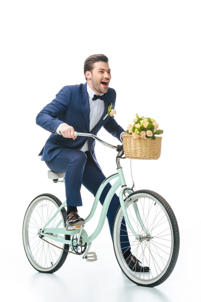 happy groom in suit riding retro bicycle with wedding bouquet in basket isolated on white - Photo, Image
