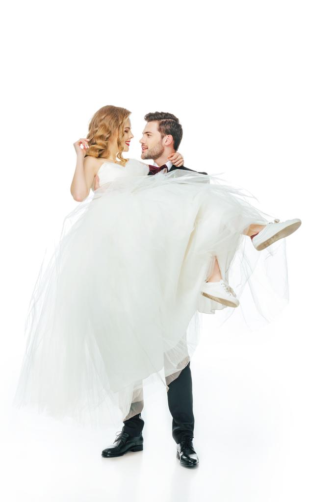 νεαρού γαμπρού κρατώντας όμορφη νύφη στα χέρια που απομονώνονται σε λευκό - Φωτογραφία, εικόνα