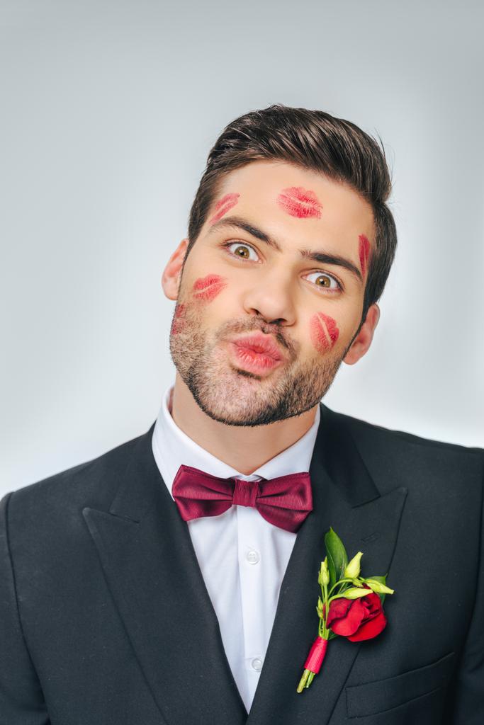 Porträt des hübschen Bräutigams im Anzug mit rotem Lippenstift im Gesicht isoliert auf grau - Foto, Bild