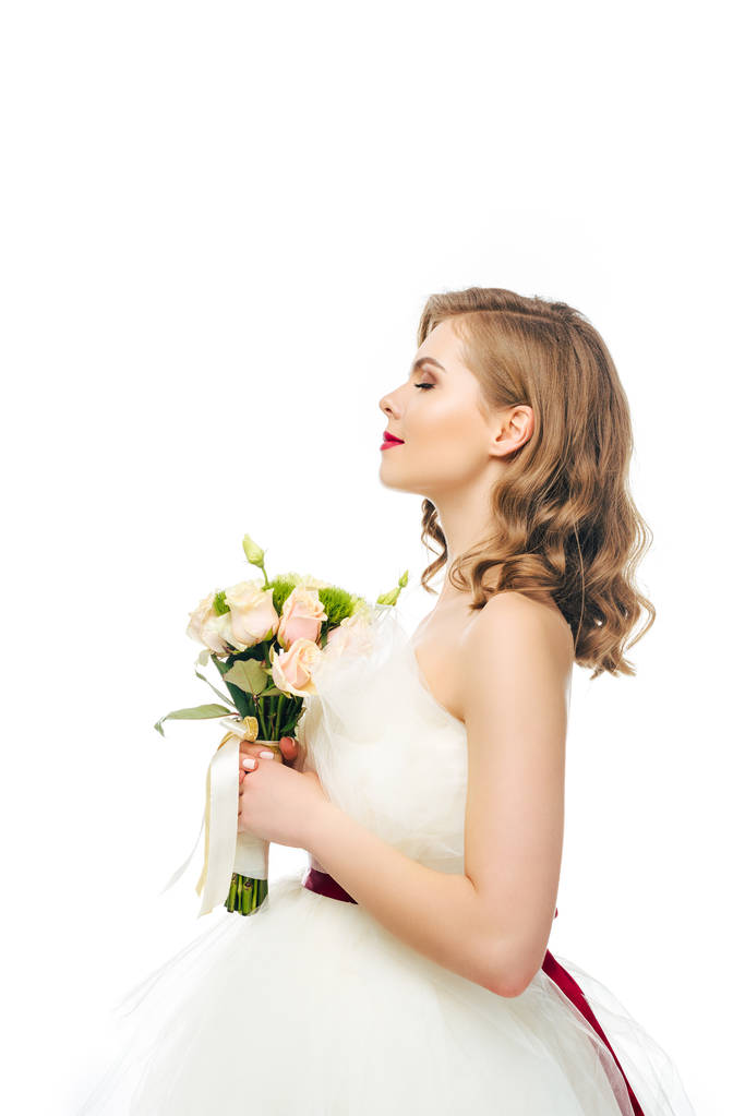 Seitenansicht der Braut im Brautkleid mit Blumenstrauß in den Händen isoliert auf weiß - Foto, Bild