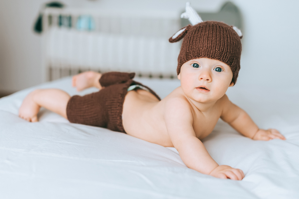 cute infant child in knitted deer costume in bed - Photo, Image
