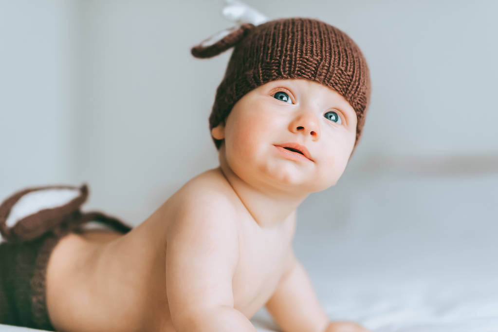 csecsemő gyerek kötött szarvas nadrág és kalap az ágyban felnézett közeli portréja - Fotó, kép