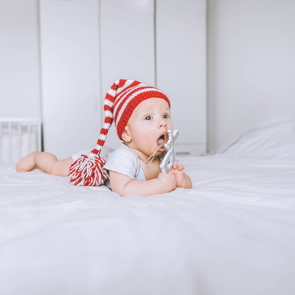όμορφο παιδί βρέφος σε ριγέ κόκκινο και λευκό καπέλο με τα ελάφια παιχνίδι στο κρεβάτι - Φωτογραφία, εικόνα