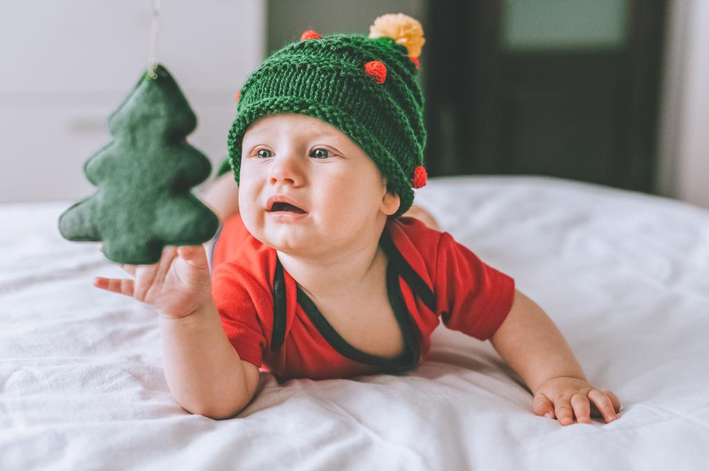 enfant en bas âge en adorable chapeau tricoté en forme d'arbre de Noël jouant avec la décoration de vacances au lit
 - Photo, image