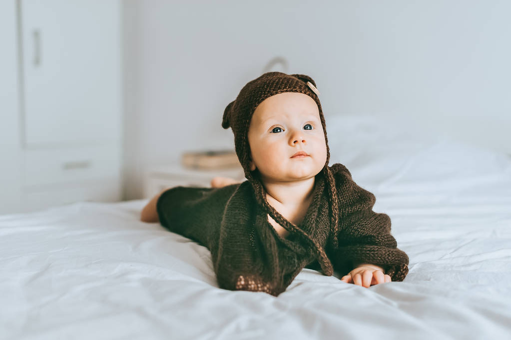 αξιολάτρευτο παιδί βρέφος σε καφέ πλεκτό καπέλο και κουβέρτα στο κρεβάτι - Φωτογραφία, εικόνα