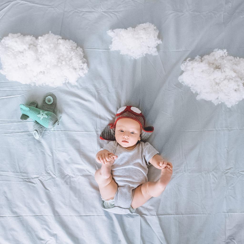 top view of adorable infant child in knitted pilot hat with toy plane surrounded with clouds made of cotton in bed - Photo, Image