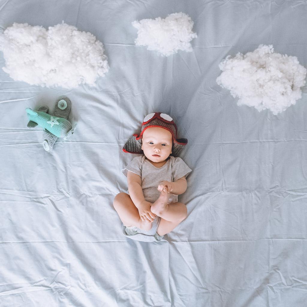 vista superior de niño de ensueño en sombrero piloto de punto con avión de juguete rodeado de nubes de algodón en la cama
 - Foto, Imagen
