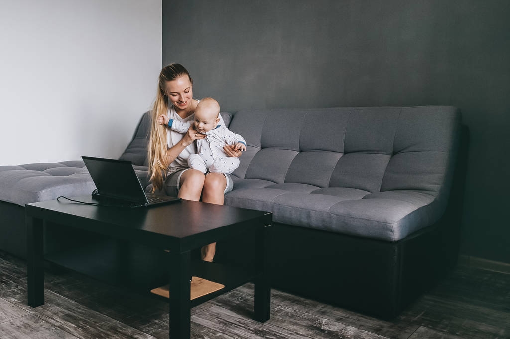 jovem mãe e seu filho bebê olhando para laptop enquanto sentado no sofá em casa
 - Foto, Imagem