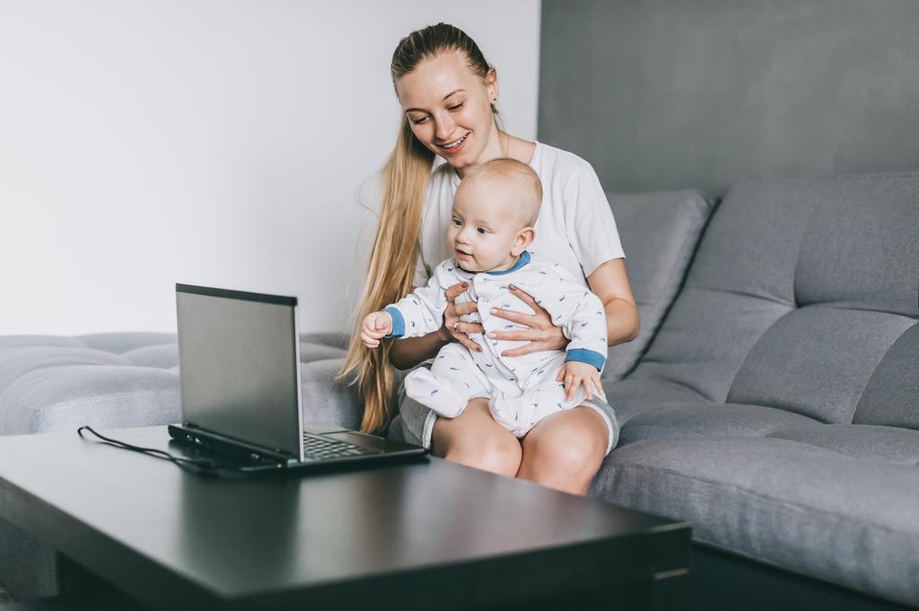 kaunis hymyilevä nuori äiti, jolla on pieni lapsi katsomassa kannettavaa tietokonetta
 - Valokuva, kuva