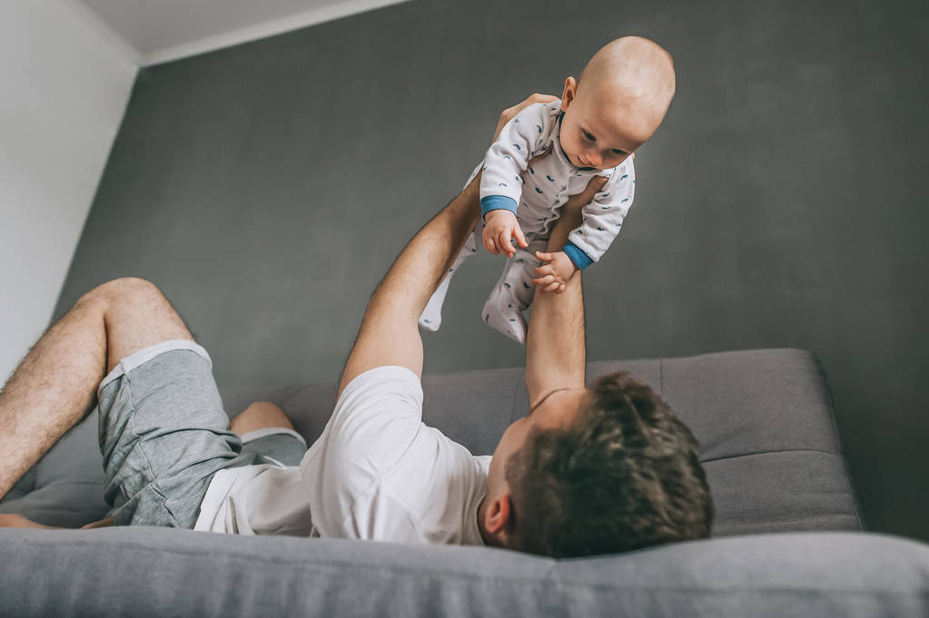 young father lying on sofa and playing with cute infant child    - Photo, Image