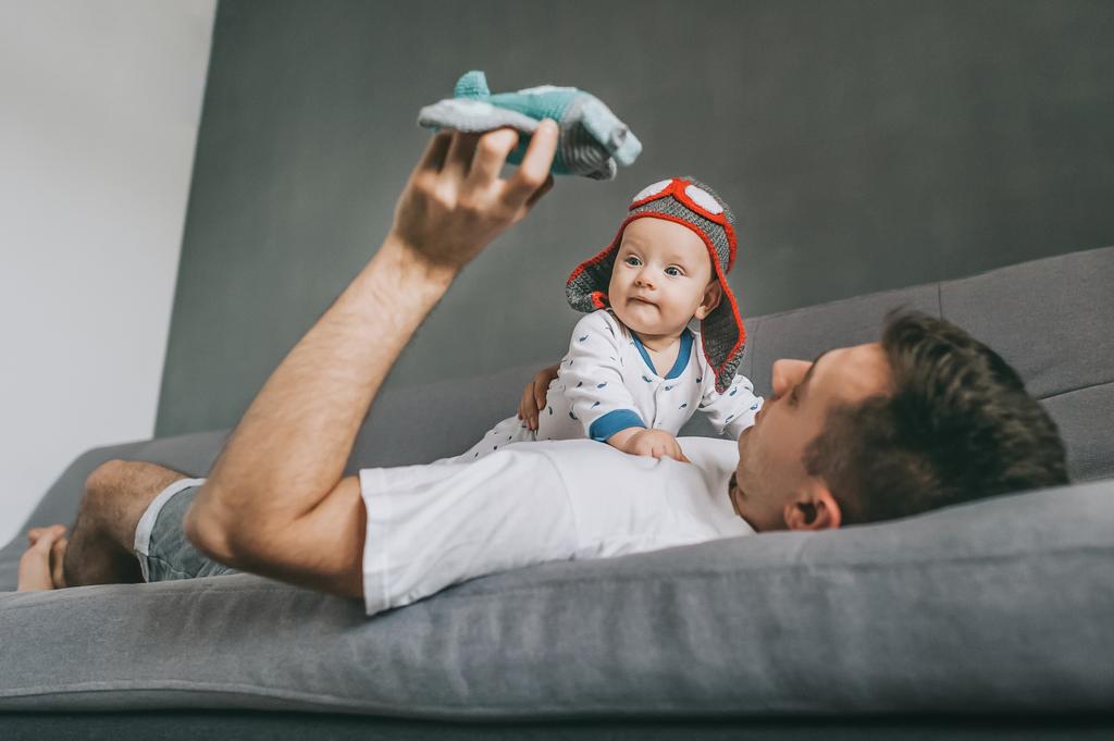 Vater hält Spielzeugflugzeug in der Hand und spielt mit entzückendem Säugling mit Strickmütze - Foto, Bild