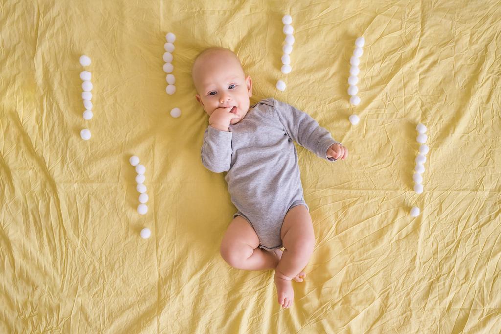 вид прелестного младенца в окружении восклицательных знаков из ватных шариков в постели
  - Фото, изображение