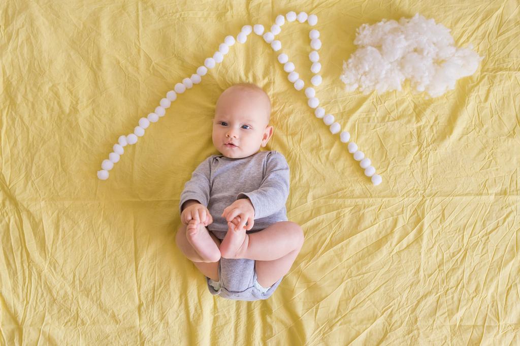 top view of adorable child lying under house roof made of cotton balls and cotton cloud on bed    - Photo, Image