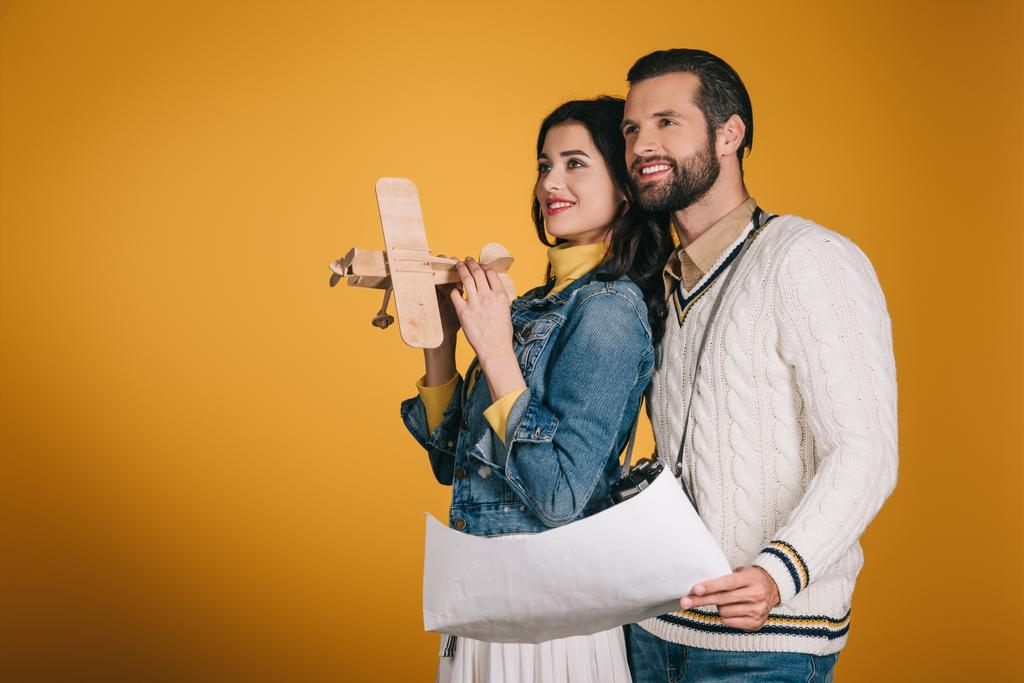 novia sosteniendo avión de madera y novio sosteniendo mapa aislado en amarillo
 - Foto, Imagen