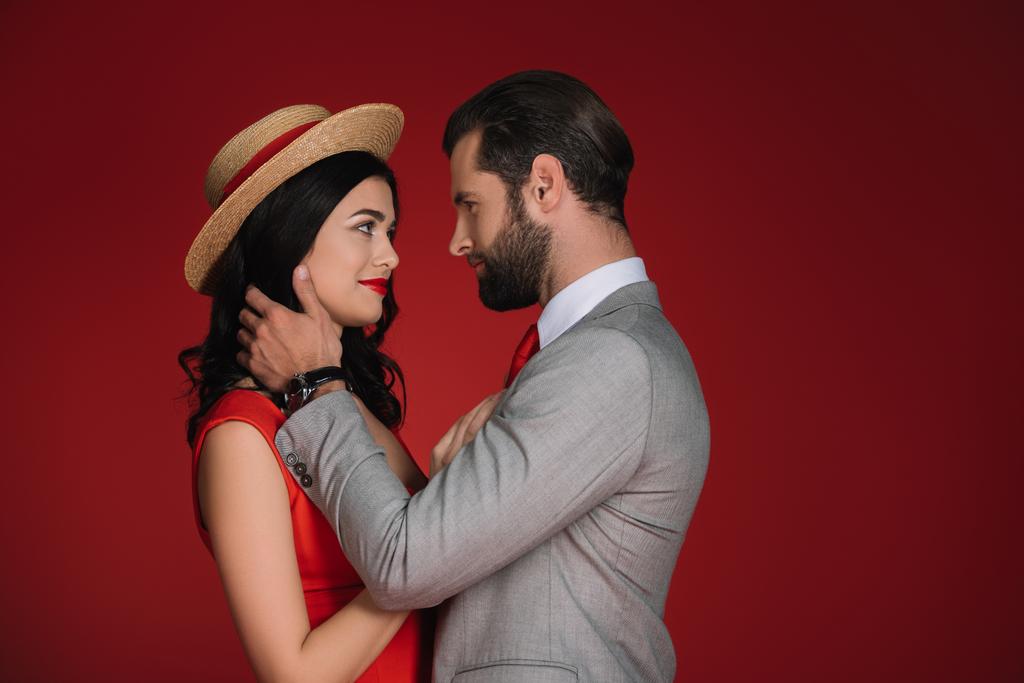 atrakcyjna para przytulanie i patrząc na siebie, na czerwonym tle - Zdjęcie, obraz