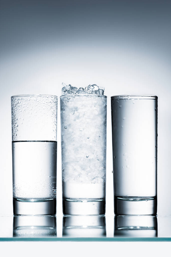 glazen water in rij- en een met ijs op het reflecterend oppervlak - Foto, afbeelding