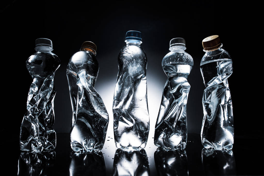 various crumpled plastic bottles of water in row on dark  - Photo, Image