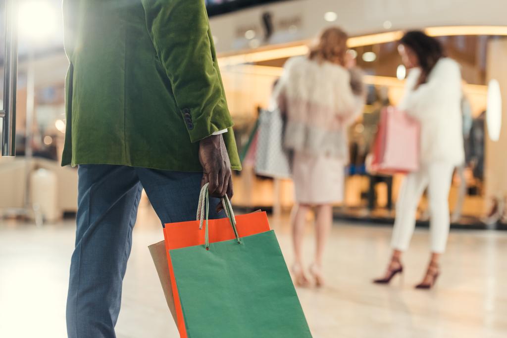 tiro recortado de homem afro-americano segurando sacos de papel enquanto caminhava no shopping
 - Foto, Imagem
