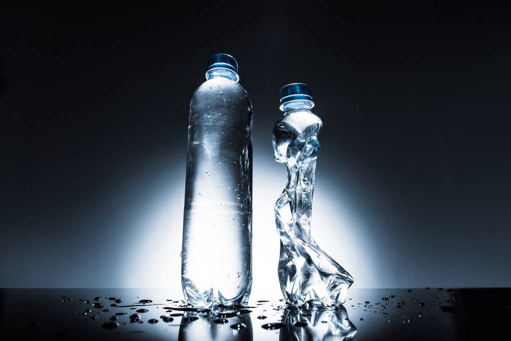 ανέγγιχτη και τσαλακωμένο μπουκάλια νερού στο σκοτάδι  - Φωτογραφία, εικόνα