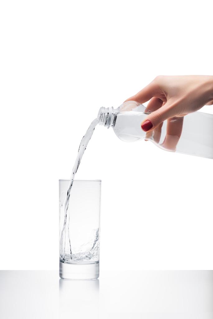 περικοπεί shot από γυναίκα ρίχνει νερό σε ποτήρι από πλαστικό μπουκάλι που απομονώνονται σε λευκό - Φωτογραφία, εικόνα