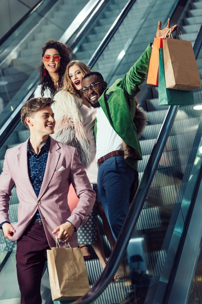 onnellinen nuori monikansallinen ostajat liukuportaat ostoskeskuksessa paketteja
 - Valokuva, kuva