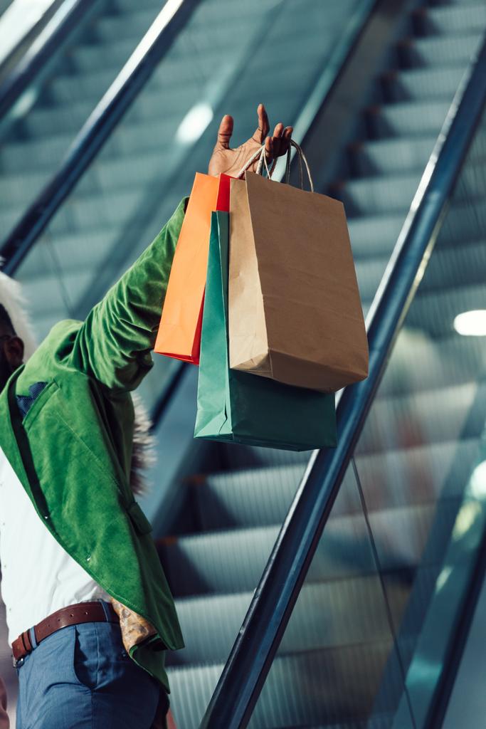 recortado disparo de hombre sosteniendo bolsas de compras mientras monta escaleras mecánicas en el centro comercial
 - Foto, imagen