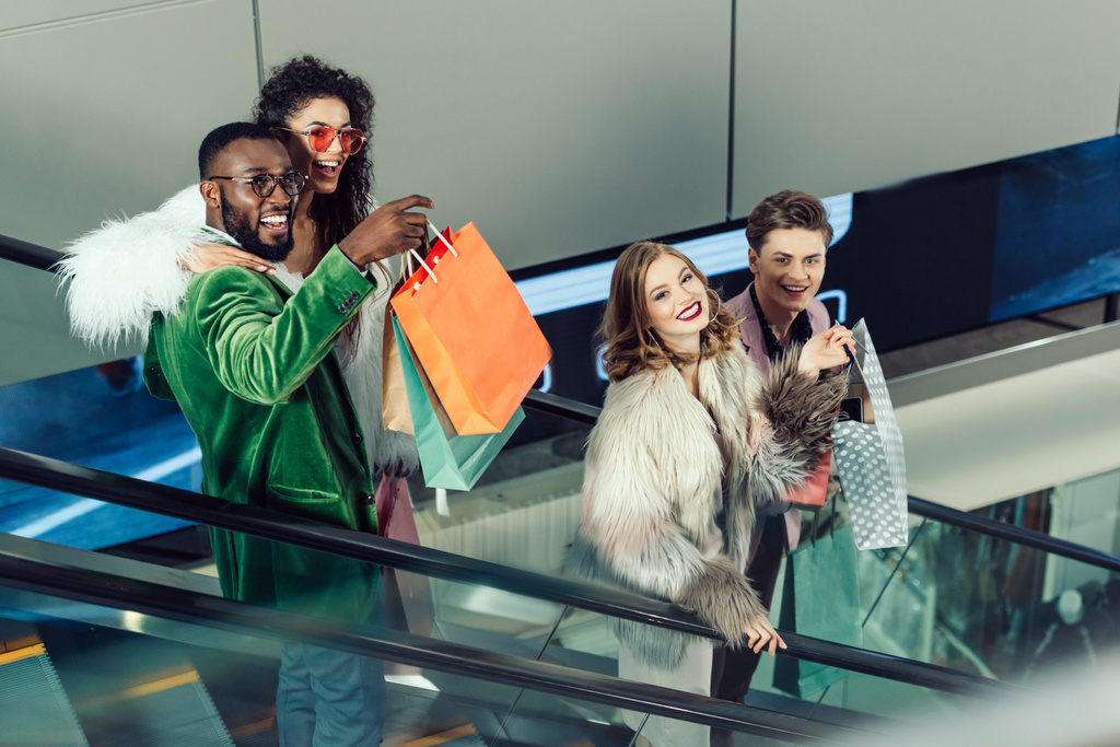grupo joven y elegante de compradores en escaleras mecánicas en el centro comercial
 - Foto, Imagen