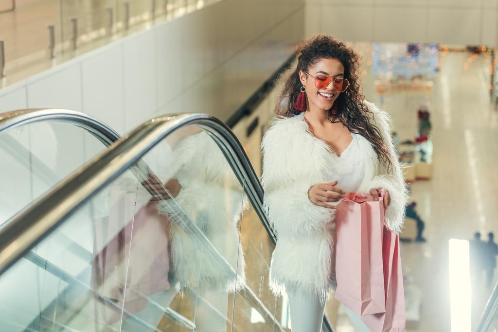 mulheres elegantes felizes olhando em saco de compras na escada rolante no shopping
 - Foto, Imagem