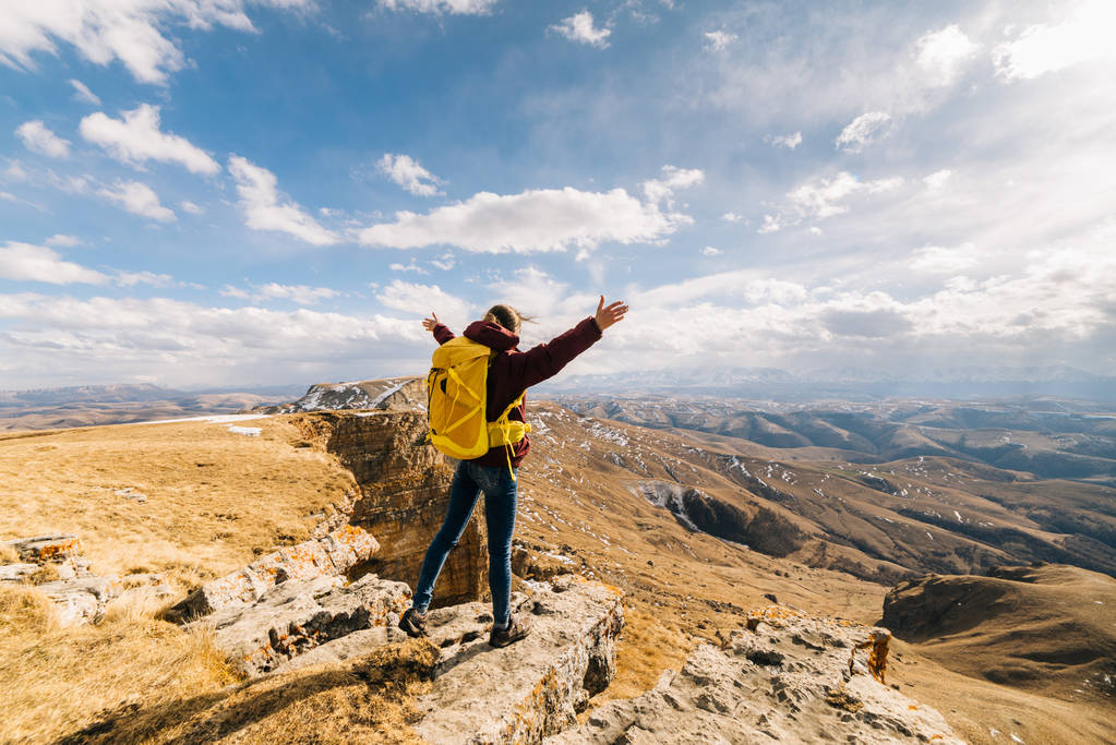 счастливая активная девушка путешествует по Кавказским горам с желтым рюкзаком, с поднятыми вверх ручками
 - Фото, изображение
