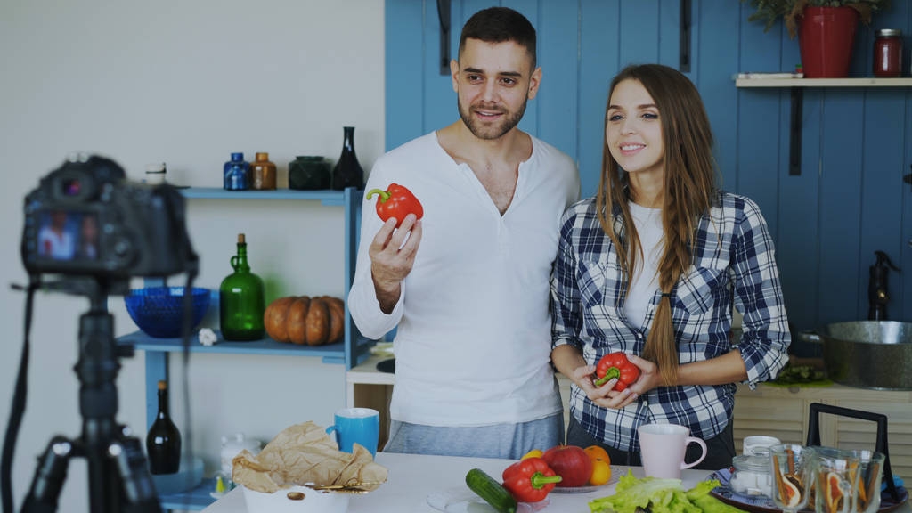 Joyeux couple attrayant enregistrement vidéo blog sur la nourriture saine végétarienne sur caméra dslr dans la cuisine à la maison
 - Photo, image