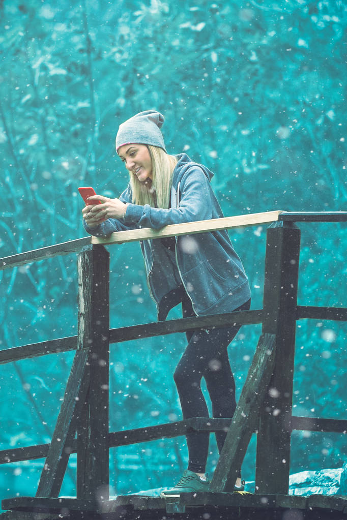 Escena de nieve de invierno de mujer usando teléfono inteligente en un pequeño híbrido de madera
 - Foto, imagen