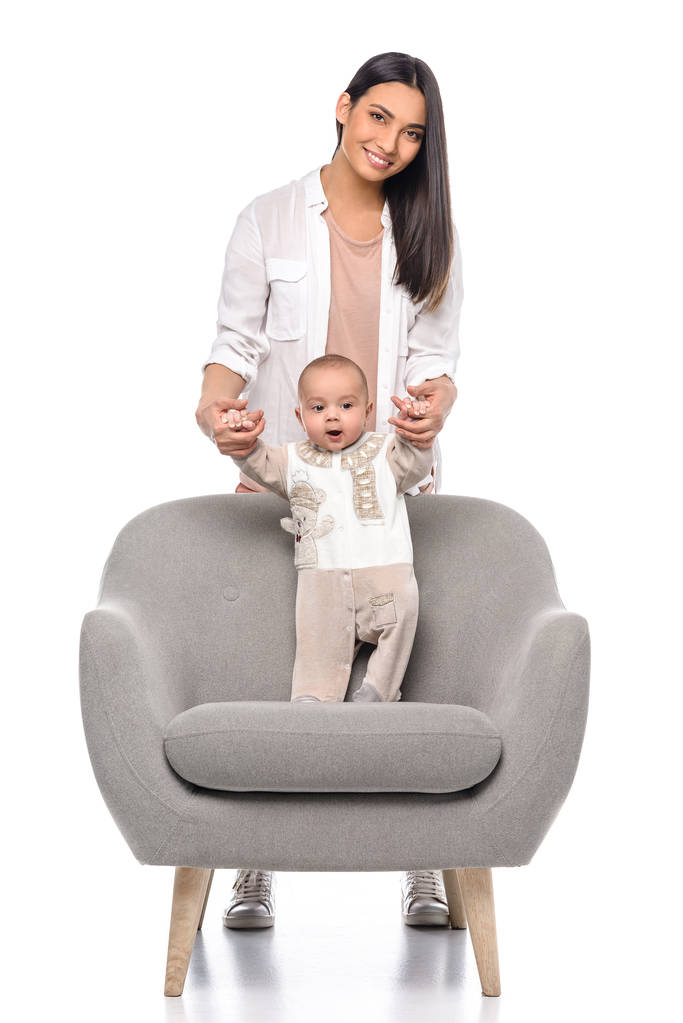 Lächelnde Frau mit kleinem Baby im Sessel isoliert auf weiß - Foto, Bild