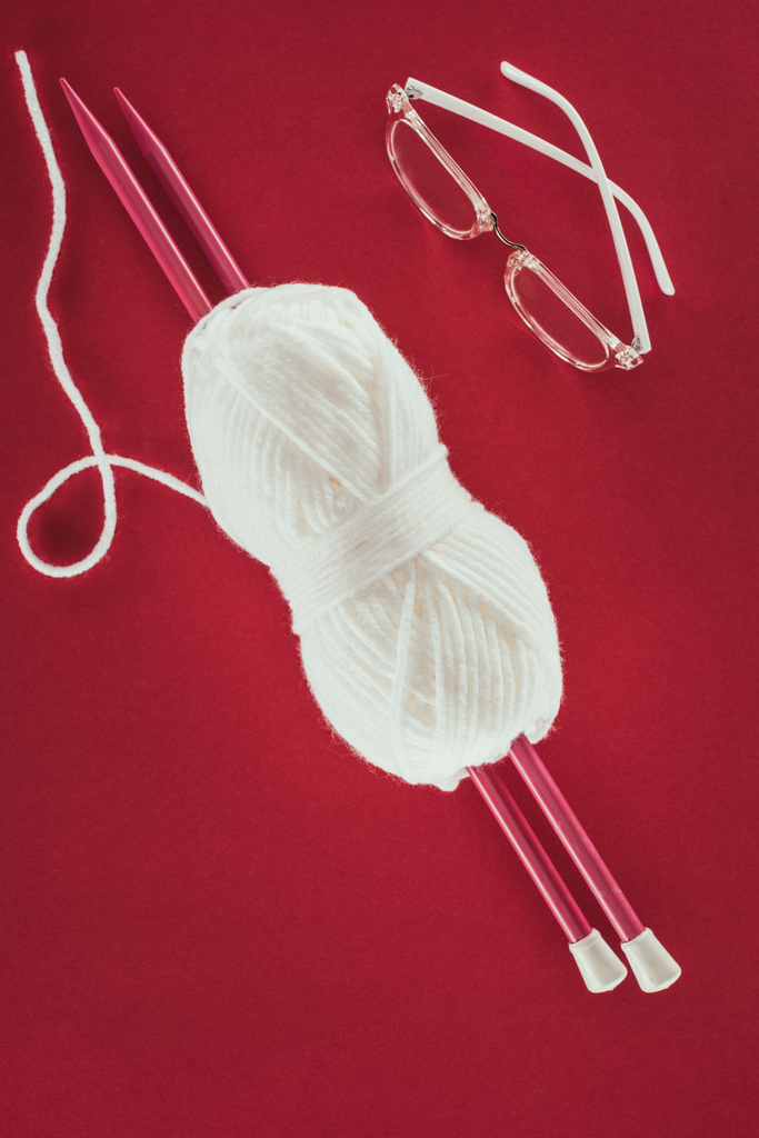 top view of eyeglasses, white yarn ball and knitting needles, isolated on red - Photo, Image
