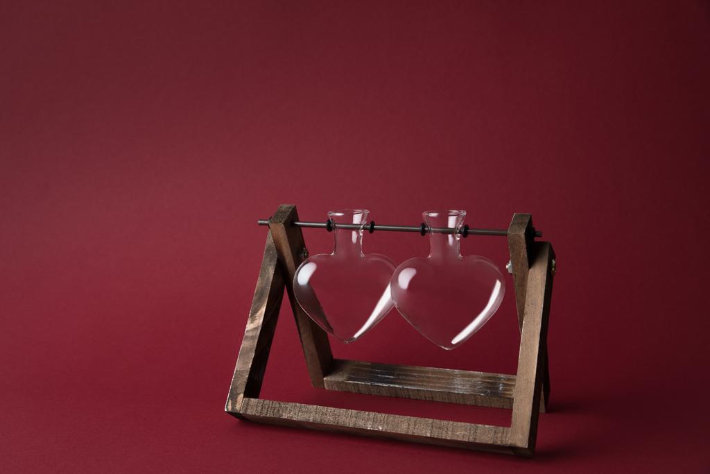 две пустые стеклянные банки в форме сердца на деревянном подставке на красном
 - Фото, изображение