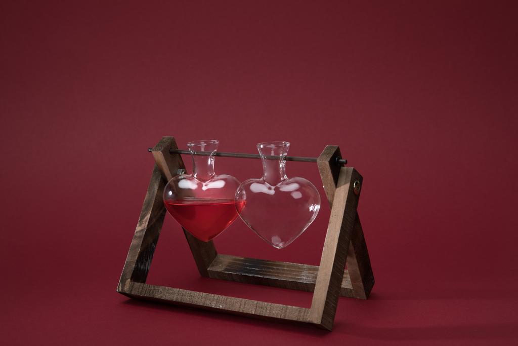heart shaped glass jar with perfume and empty glass jar on wooden stand on red - Photo, Image