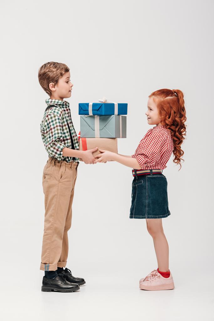 vista lateral de adorables niños felices sosteniendo regalos aislados en gris
  - Foto, imagen
