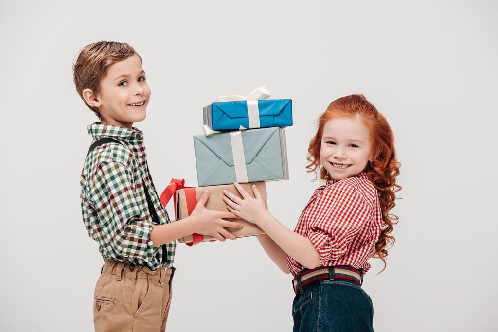 χαριτωμένα παιδάκια κρατώντας κουτιά δώρων και να χαμογελά στη φωτογραφική μηχανή που απομονώνονται σε γκρι - Φωτογραφία, εικόνα