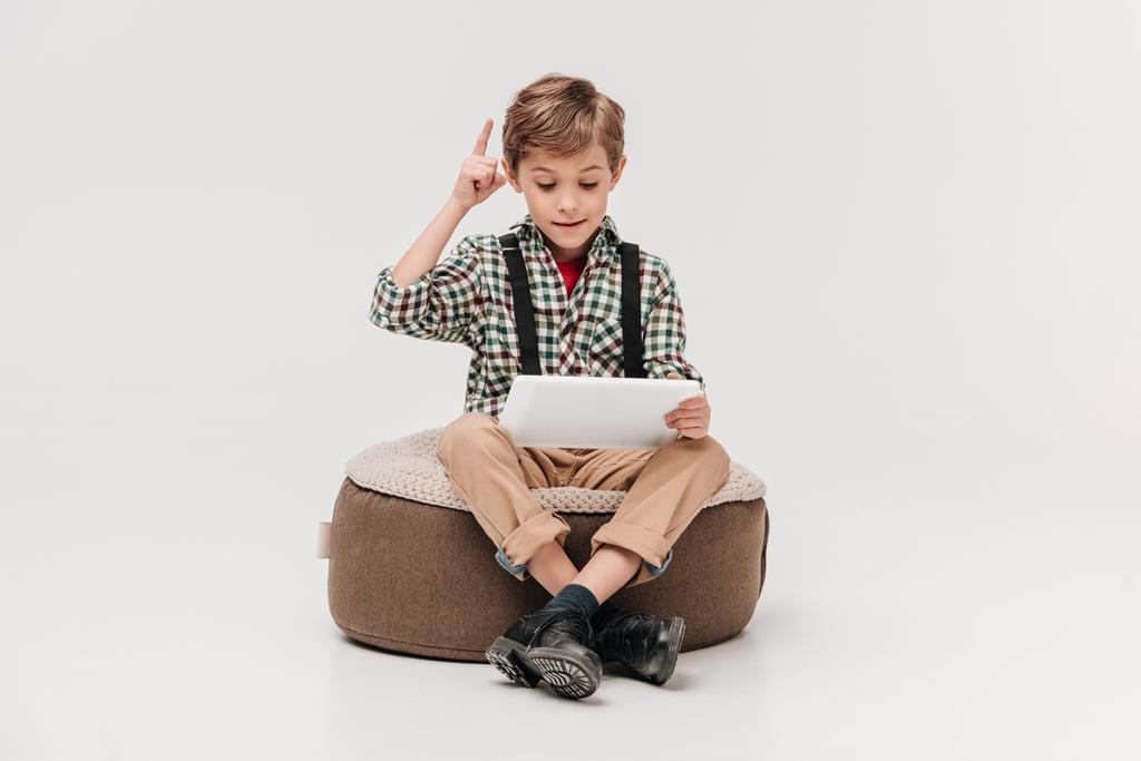 lindo niño usando tableta digital y apuntando hacia arriba con el dedo aislado en gris
 - Foto, Imagen