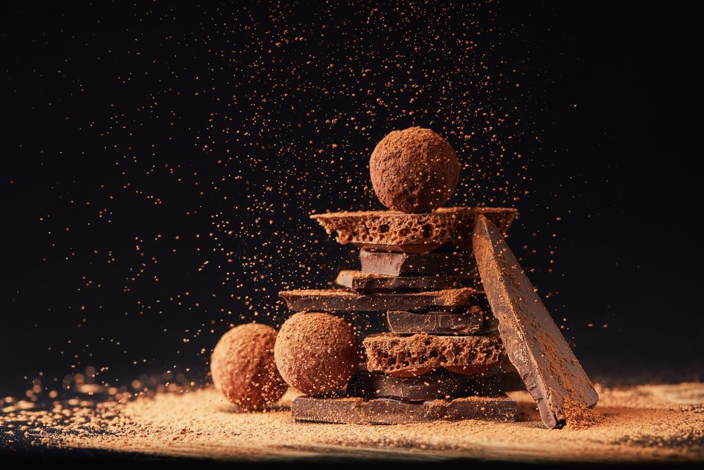 vista ravvicinata di disposizione di tartufi e barrette di cioccolato con cacao in polvere su nero
 - Foto, immagini